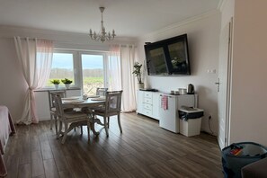 Una cocina con una mesa de comedor, sillas, una araña, un televisor y una ventana con cortinas.
