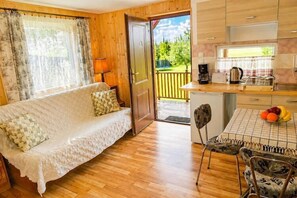 A cozy room with a sofa, a dining table with fruit, a coffee maker, and a view of a garden. - Holiday cottage in Wisełka (Wisełka)