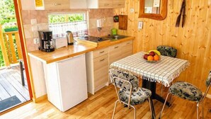 Una cucina funzionale con frigorifero, piano cottura e lavello. È presente un tavolo con sedie e una ciotola di frutta.