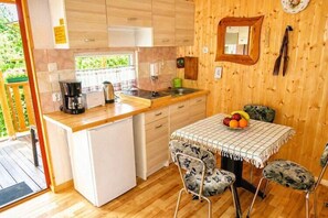 A compact kitchen with a refrigerator, stove, and sink. There is a dining table with chairs and a fruit bowl. - Holiday cottage in Wisełka (Wisełka)