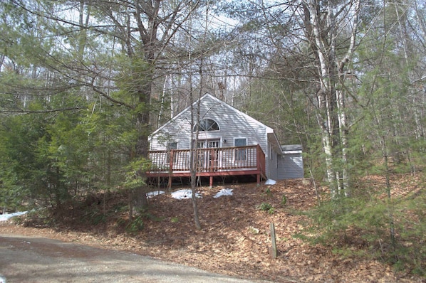 Une cabane dotée d’une terrasse, entourée d’arbres et bordée d’une zone boisée.