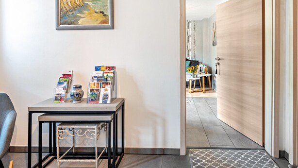 A room with a table displaying brochures and a framed painting of a coastal scene. - Apartment "Weinbergschnecke" with Private Terrace and Wi-Fi (Efringen-Kirchen)