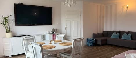A living room with a flat-screen TV, a dining table with chairs, a sofa, and a chandelier.