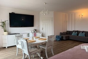 Een woonkamer met een flatscreen televisie, een eettafel met stoelen, een bank en een kroonluchter.
