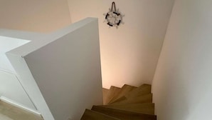 A staircase with a wall-mounted light fixture and a white wall. - Ferienwohnung in Petersdorf auf Fehmarn (Petersdorf)