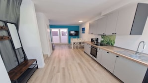 A modern kitchen with a dining area, a TV, and a view through a glass door. - Ferienwohnung in Petersdorf auf Fehmarn (Petersdorf)