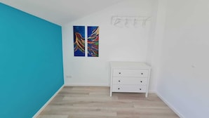 A room with a white dresser, two colorful paintings on the wall, and a blue accent wall. - Ferienwohnung in Petersdorf auf Fehmarn (Petersdorf)