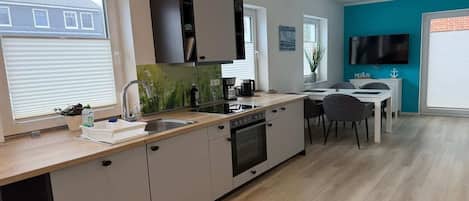 A modern kitchen with a built-in oven, a dining area with a table and chairs, and a TV mounted on the wall.