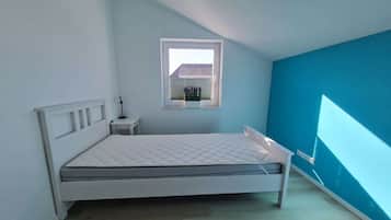 A bedroom with a bed, a small bedside table, a window, and a wall with a blue accent.