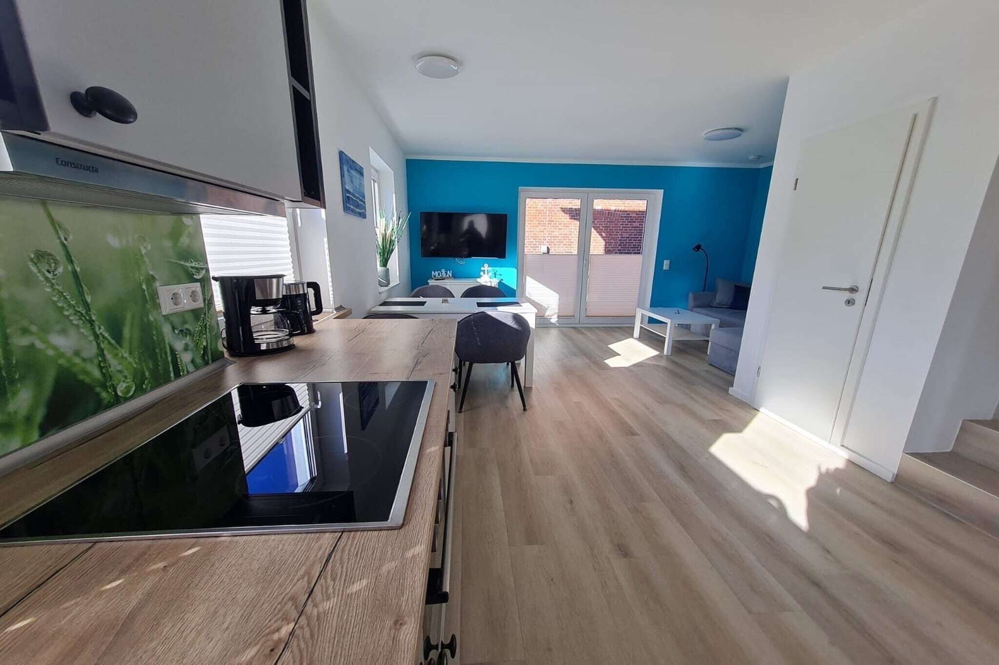 A modern kitchen with a large flat-screen TV, a coffee machine, and a dining area with a table and chairs.