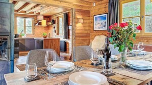 Interior d'una cabana de fusta amb taula de dinar per a quatre, zona de cuina i finestra gran amb vistes.