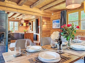 Interior de una cabaña de madera con una mesa de comedor para cuatro personas, una zona de cocina y un amplio ventanal con vistas.