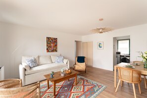 Una sala de estar con sofá, mesa de centro y sillas, un comedor con mesa y sillas, y una cocina al fondo.