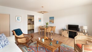 Ein Wohnzimmer mit einer Couch, Sesseln, einem Couchtisch, einem Fernseher und einem Essbereich mit Tisch und Stühlen.