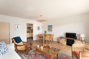 Una sala de estar con un sofá, sillas, una mesa de centro, un televisor y un comedor con una mesa y sillas.