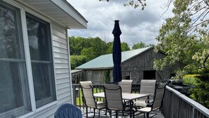 Una terraza de madera con mobiliario exterior, incluyendo sillas y una mesa, y un paraguas cubierto.