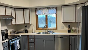 Una cocina moderna con gabinetes grises, un refrigerador de acero inoxidable, un horno integrado y un ventanal con vistas a árboles.