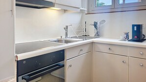 A kitchen with a sink, stove, cabinets, and a window with a view of palm trees. - Residenza Corallo by Interhome (Ascona)