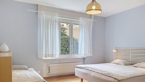 A bedroom with two beds, a window with curtains, a radiator, and a hanging light fixture. - Residenza Corallo by Interhome (Ascona)
