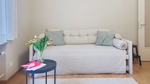 A neutral-colored sofa with two cushions, a small round table with a vase of flowers, and a white rug on a wooden floor. - Residenza Corallo by Interhome (Ascona)