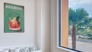 A room with a window, a shelf with white cups, and a wall-mounted sign reading 'NEGRONI'. - Residenza Corallo by Interhome (Ascona)