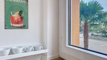 Une pièce avec une fenêtre, une étagère où sont posées des tasses blanches et un panneau fixé au mur sur lequel on peut lire « NEGRONI ».