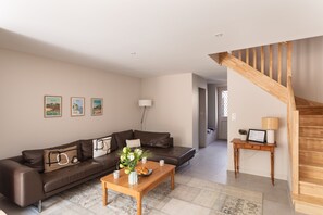 Una sala de estar con un sofá de cuero marrón, una mesa de centro de madera y una escalera.
