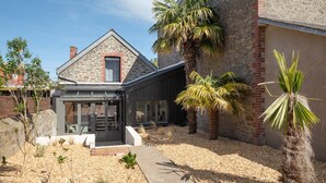 Una casa moderna con fachada de piedra, puerta de entrada de vidrio y un pequeño jardín con palmeras.