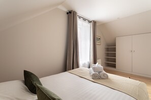 Een slaapkamer met een bed, kussens, een opgerolde handdoek, een kledingkast en een raam met gordijnen.
