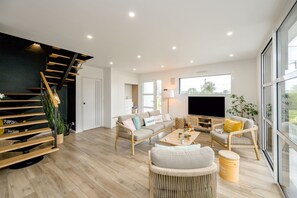Uma sala de estar ampla com escada, sofás, mesa de centro e televisão.