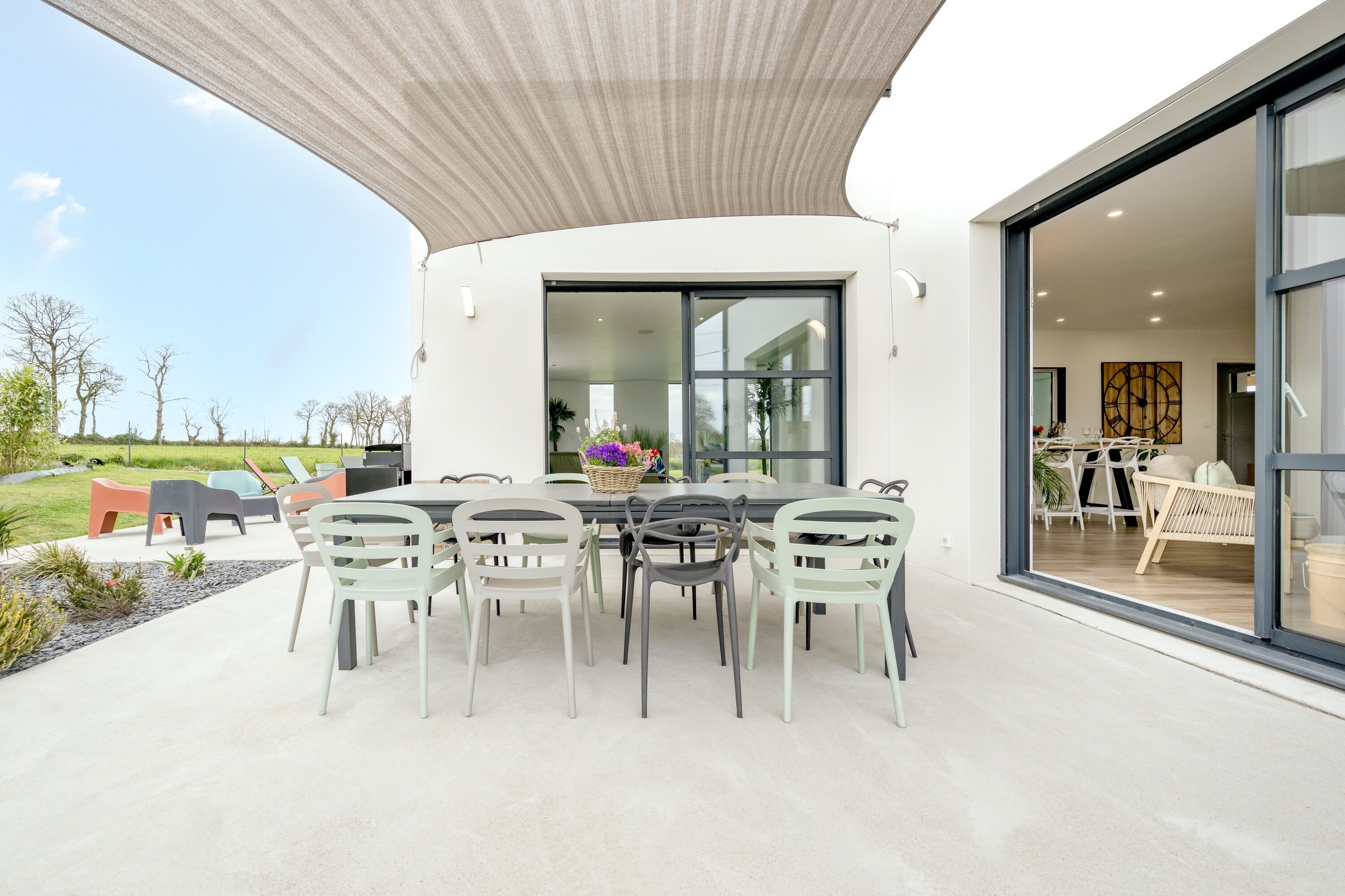 An outdoor dining area with a table and chairs, a basket of flowers, and a view of the landscape.
