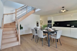 A modern kitchen with white cabinets, a black countertop, and a dining area with a table set for four. - Résidence Des Champs sur Mer - À 400 m de la plage (Dinard)