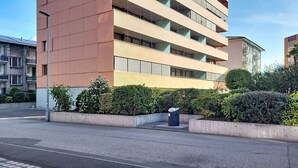 A multi-story building with a modern architectural design, featuring balconies and a parking area with a trash bin. - Residenza Eride - Apt.4 by Interhome (Locarno)