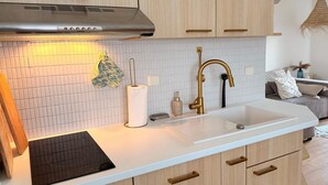 A modern kitchen with a white countertop, wooden cabinets, a stainless steel range hood, and a gold faucet. - Ferienwohnung in Lemkenhafen für 3 Gäste (Lemkenhafen)