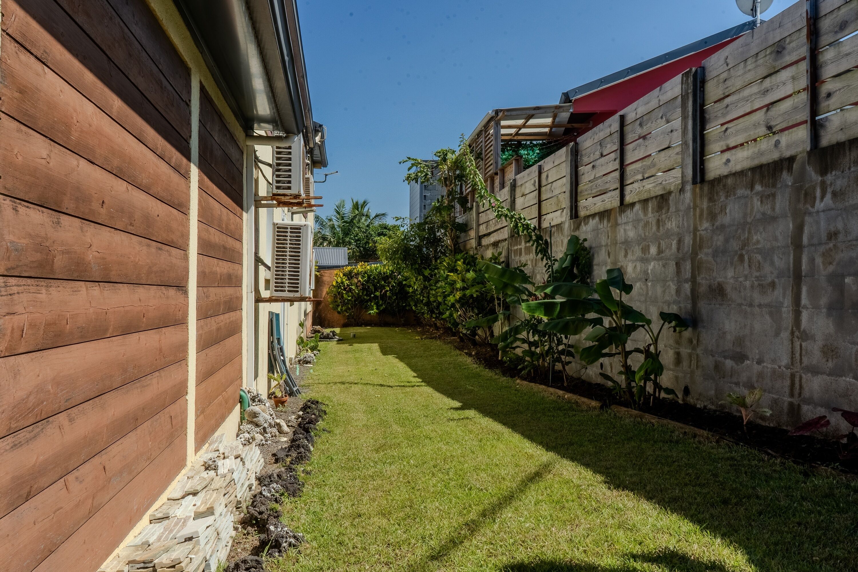 Un jardin avec une clôture en bois, une pelouse verdoyante et un mur en béton.