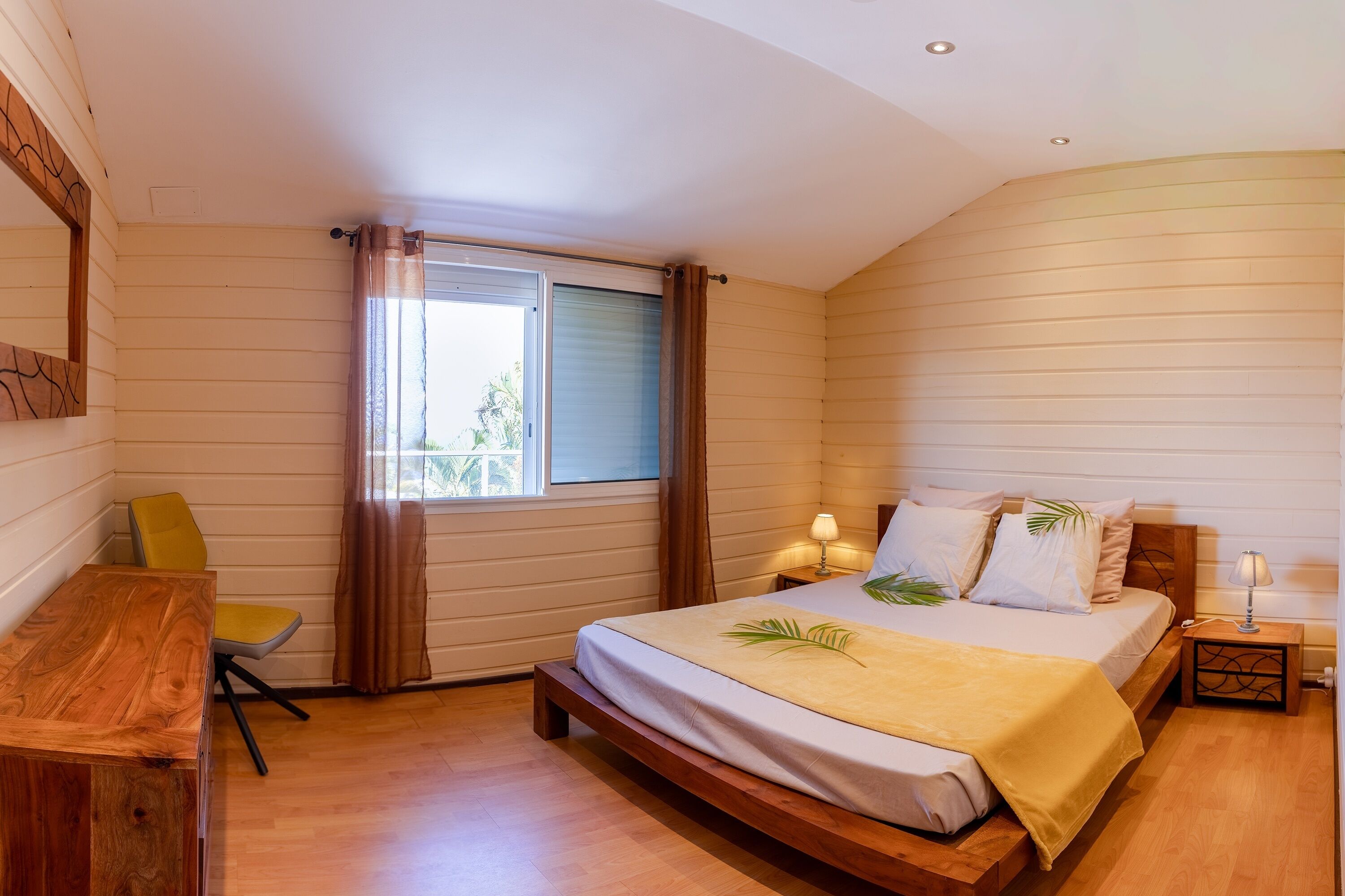 A bedroom with a wooden bed, a desk, a chair, and a window with curtains.