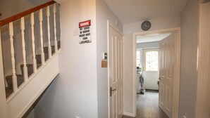 Un couloir avec un escalier, une porte ornée d’un panneau d’avertissement et une horloge au mur.