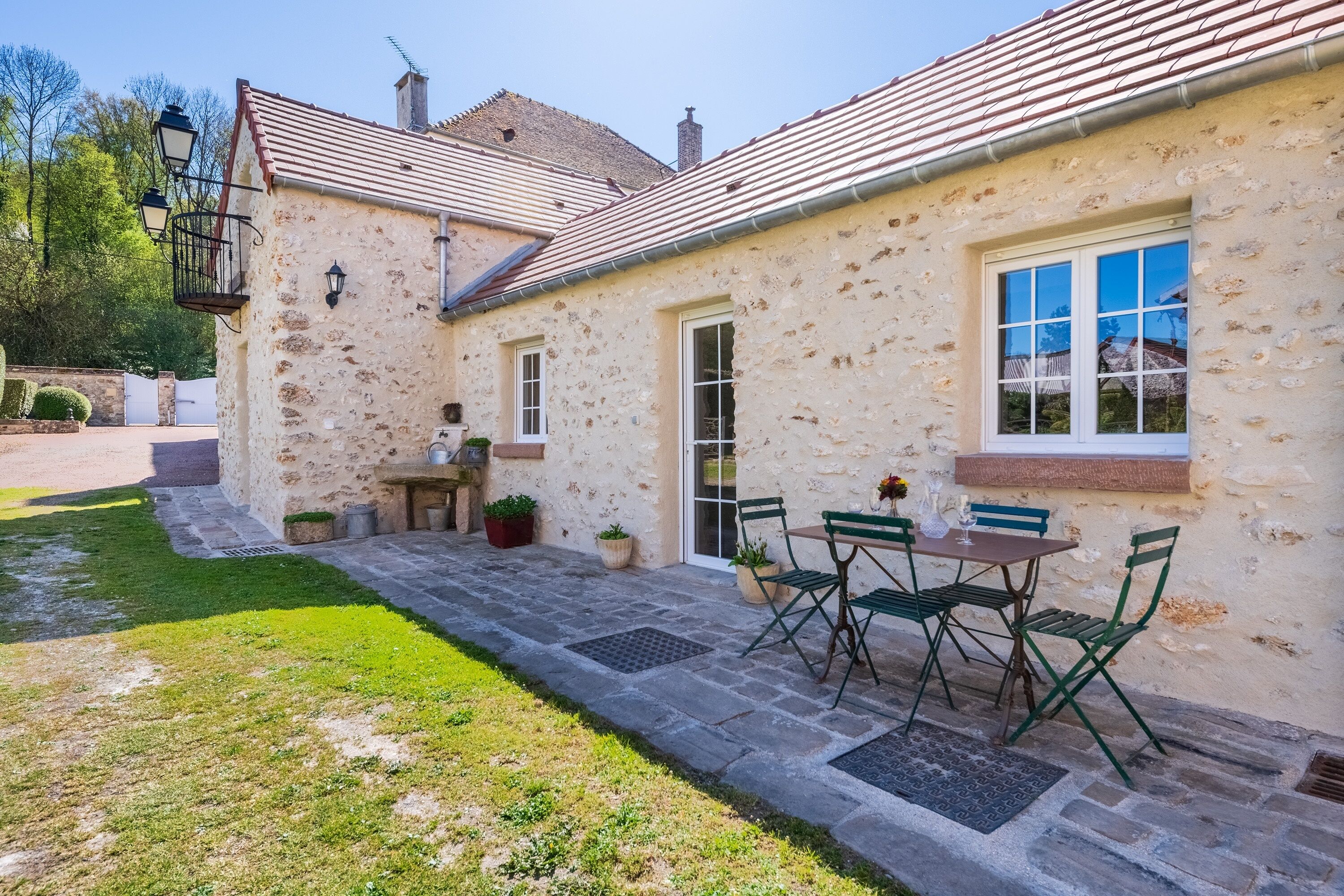 A stone building with a tiled roof, a patio with a table and chairs, and a window with a view.