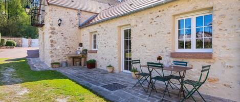 A stone building with a tiled roof, a patio with a table and chairs, and a window with a view.