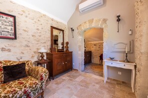 Une pièce avec un mur en pierre, un meuble en bois, une console blanche et un canapé à motifs floraux.