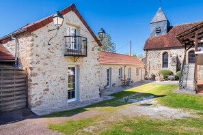 Un bâtiment en pierre doté d’un balcon, une église avec un clocher et une cour dallée.