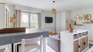 Ein Zimmer mit Esstisch, Sofa, Wandfernseher und einem fenster mit Vorhängen.