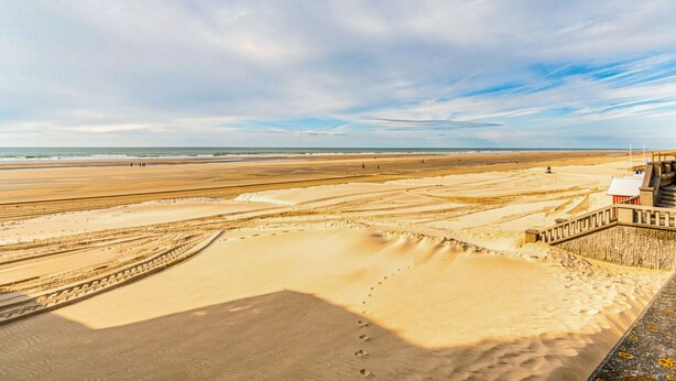 Ein Strand mit einem hölzernen Promenadenweg, Sanddünen und einem klaren Himmel.