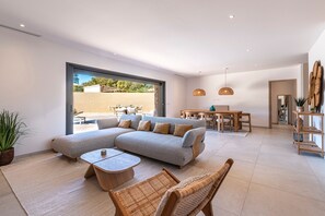 A spacious living area with a sectional sofa, a dining table, and a large window. - La Villa Frassolo - Belle terrasse avec piscine (Lecci)