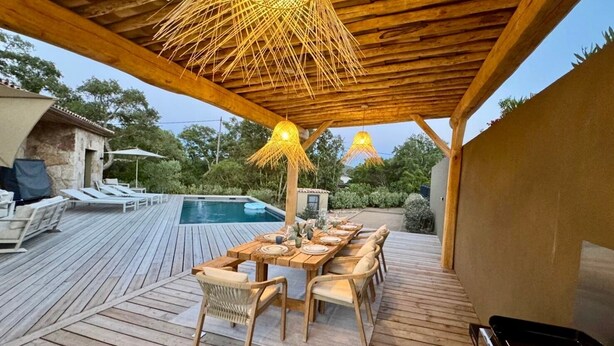 Eine Terrasse im Freien mit Pool, Holzmöbeln und hängenden Lampen.