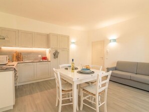 A compact kitchen with a dining table and chairs, a grey sofa, and a door. - Nuraghi by Interhome (Arzachena)