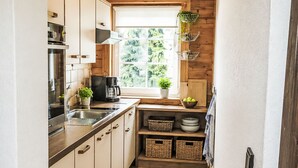 Eine kompakte Küche mit Fenster, Holzschränken, einer Kaffeemaschine und einem Blumentopf.