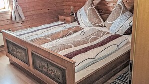 Uma cama de madeira com colcha e almofadas estampadas, uma mesa de cabeceira com abajur e uma janela com cortinas.