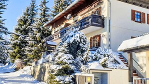 Um edifício com vários andares, varanda, árvores cobertas de neve e céu claro.