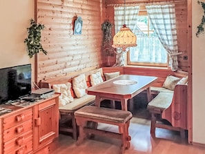 A cozy cabin interior with a wooden wall, a bench seating area, a table, and a television.